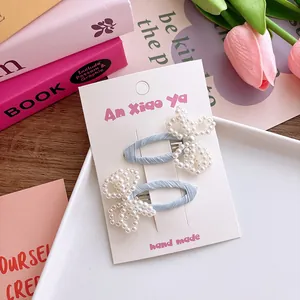 Détail de barrettes en tissu bleu avec nœud en perles sur carte de présentation rose