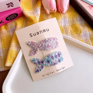 Detail of two glitter mermaid tail hair clips in pink and blue on a display card