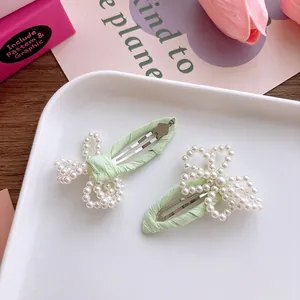 Détail de barrettes à perles avec tissu vert menthe posées sur un plateau blanc