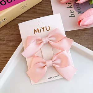 Detail of sweet pink satin bow hair clips displayed on a branded card with tulip background