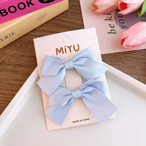 Close-up of a pair of light blue satin ribbon bow hair clips on a branded display card