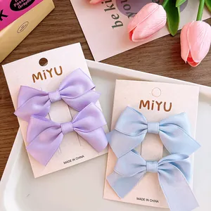 Close-up of pastel satin bow hair clips in lavender and blue on card packaging