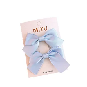 Pair of light blue satin ribbon bow hair clips for girls on a white display card