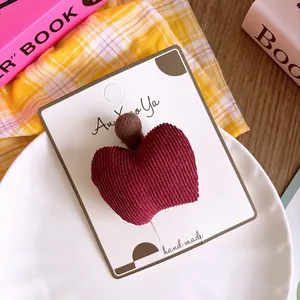 Detalle de una pinza para el pelo de manzana roja en pana sobre tarjeta de presentación
