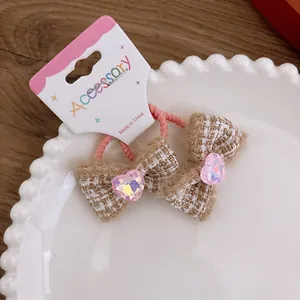 Detail view of pink tweed bow hair tie with heart-shaped crystal on white ceramic tray