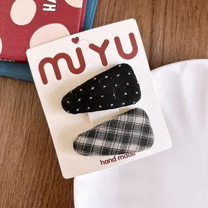 Detail view of two fabric-wrapped hair clips with polka dot and plaid patterns on card