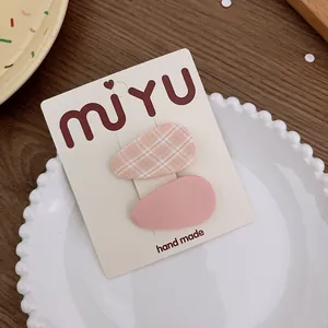 Detalle de pinzas para el cabello en tela a cuadros naranja y rosa en plato de porcelana