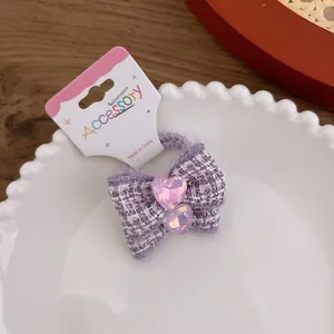 Detailed macro view of purple plaid bow hair tie with pink heart crystals on white plate
