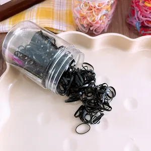 Detail of high elasticity black rubber hair ties spilling from a storage jar onto a tray