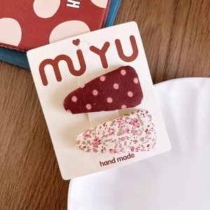 Detail of floral and polka dot fabric hair clips displayed on handmade card packaging