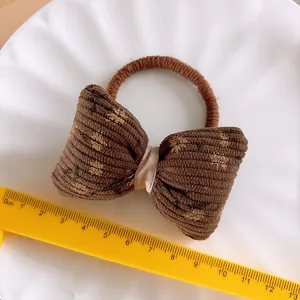 Detail eines kaffeebraunen Blumen-Cord-Haargummis mit Gummiband auf weißem Teller