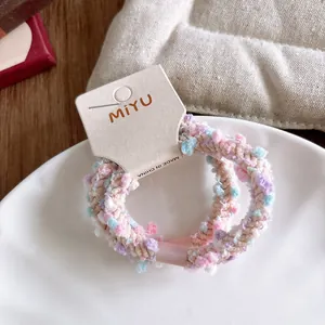 Détail des élastiques à cheveux tissés pastel avec pompons en peluche colorés sur plateau