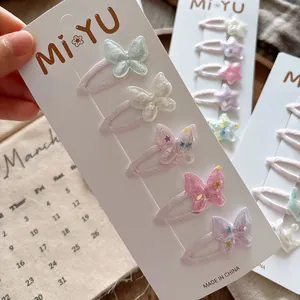 Détail de barrettes papillon pailletées en couleurs pastel sur carte de présentation