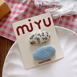 Close-up of sweet floral fabric and blue tweed oval hair clips on a white display card