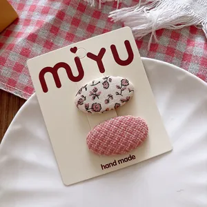 Detail of sweet floral and pink tweed fabric oval hair clips on a branded display card