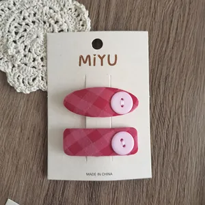 Dettaglio di due fermagli per capelli in tessuto scozzese rosa con bottoni su carta