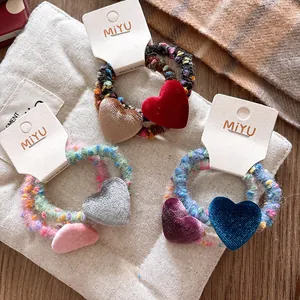 Vista dettagliata di tre elastici per capelli a cuore in velluto con etichette MIYU
