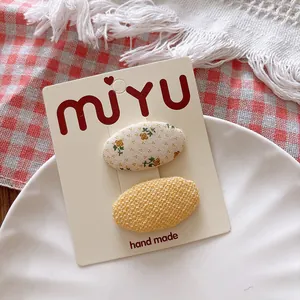 Detailed view of floral and yellow fabric oval hair clips on a branded display card