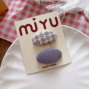 Detailed view of floral and purple woven oval hair clips on a branded display card