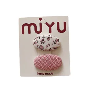 Floral and woven fabric oval hair clips for girls set on a white brand card display