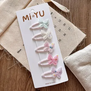 Vue détaillée de cinq barrettes papillon macaron en tissu scintillant sur bois rustique