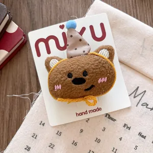 Close-up of a plush bear hair clip with a polka-dot hat on a branded display card