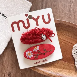 Macro detail of red bow hair clip with heart charm and daisy embroidery on a display card