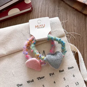 Dettaglio di ciondoli a cuore in velluto su elastici per capelli in maglia colorata