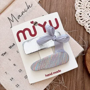 Detailed view of silver bow and woven hair clips set on handmade packaging card