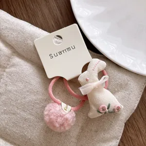 Close-up of pink velvet hair ties with embroidered rabbit charm and soft pom-pom