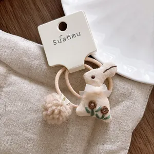 Detailed view of plush rabbit hair ties with floral embroidery on cream display card