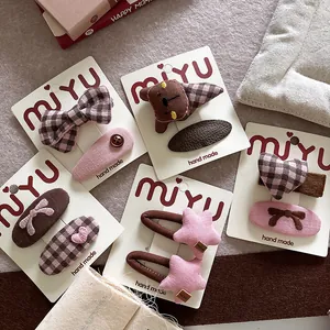 Detail of handmade bow hair clips and brown bear hairpins in pink plaid on felt background