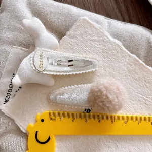 Detail of bunny rabbit hair clip and beige fluffy pom pom set on velvet fabric background