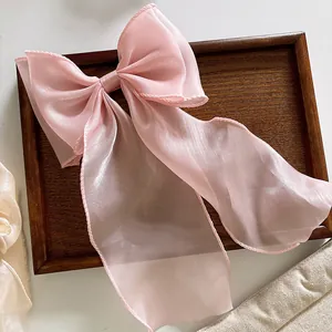 Detail of pink organza oversized bow hair clip with silky texture on dark wood tray
