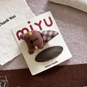Detailed view of handmade brown fabric bear hair clip and leather hairpins on card