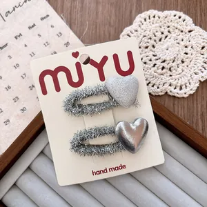 Close-up of two silver heart hair clips with glitter finish on a handmade card display