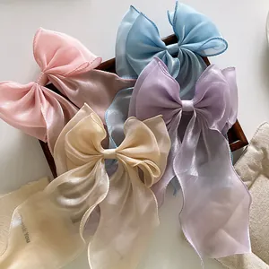 Close-up of organza bow hair clips in pink, blue, purple, and cream on a wooden tray