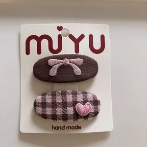 Detail of fabric hair clips with embroidered bow and heart on a display card