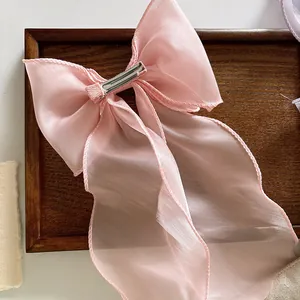 Pink sheer organza bow hair clip with long ribbons and metal clip on wooden background