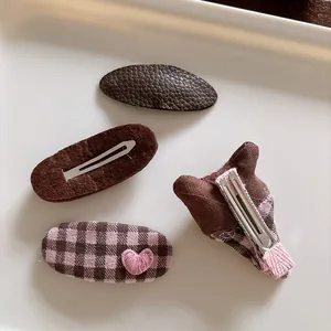 Detail of four-piece hair clip set featuring brown faux leather and pink plaid fabric