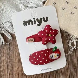 Détail de barrettes à pois rouges avec broderie de chat animé sur carte de présentation