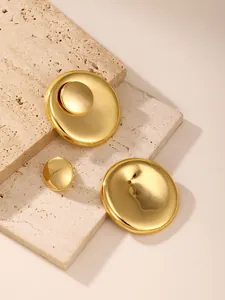 Detailed macro view of high-polished gold-tone circular earrings on beige stone backdrop