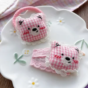 Detail of pink plaid bear hairclip and scrunchie with lace trim on a white plate