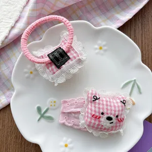 Detail of pink plaid bear hair clip and scrunchie with lace trim on a white plate