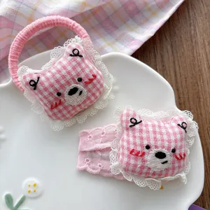 Close-up of pink plaid bear hairclip and hair tie with white lace edges on a tray