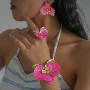Dettaglio di un set di gioielli orchidea in smalto rosa vivace indossato in stile vacanza.