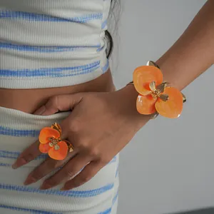 Dettaglio ravvicinato del set anello e bracciale con fiori in smalto arancione vivace.