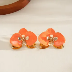 Dettaglio di un fiore in smalto arancione su un bracciale rigido dorato in stile resort.