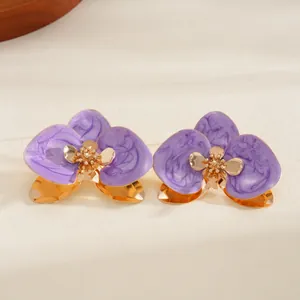 Dettaglio dei fiori in smalto viola marmorizzato su un bracciale rigido dorato aperto.