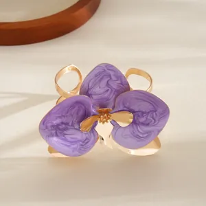 Dettaglio del bracciale rigido dorato con un grande fiore viola con effetto smalto